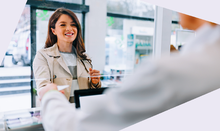 Eine Person steht in einer Apotheke und übergibt ein Rezept an einen Apothekenmitarbeitenden. Dieser steht hinter dem HV und streckt die Hand aus um das Rezept entgegen zu nehmen.
