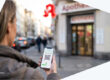 Eine Frau steht vor einer Apotheke und hält ein Smartphone mit einem QR-Code in der Hand, mit einem digitalen Rezept.