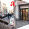 Eine Frau steht vor einer Apotheke und hält ein Smartphone mit einem QR-Code in der Hand, mit einem digitalen Rezept.