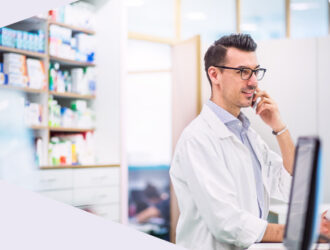 Apotheker im weißen Kittel telefoniert in einer modernen Apotheke am Verkaufstresen.
