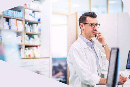 Apotheker im weißen Kittel telefoniert in einer modernen Apotheke am Verkaufstresen.