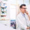 Apotheker im weißen Kittel telefoniert in einer modernen Apotheke am Verkaufstresen.