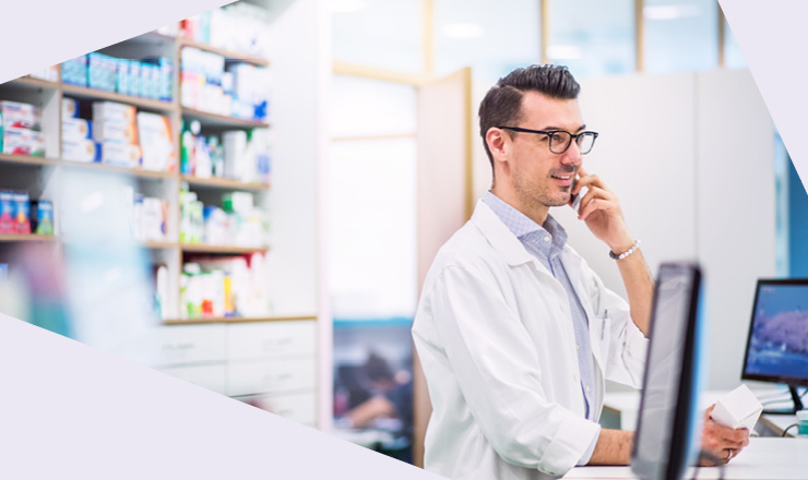 Apotheker im weißen Kittel telefoniert in einer modernen Apotheke am Verkaufstresen.